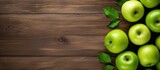 A captivating top down view of a wooden background featuring an arrangement of crisp green apples and ample free space for text