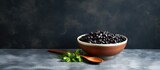 A copy space image of black beans in a ceramic bowl with a plastic spoon resting on a dark marble surface