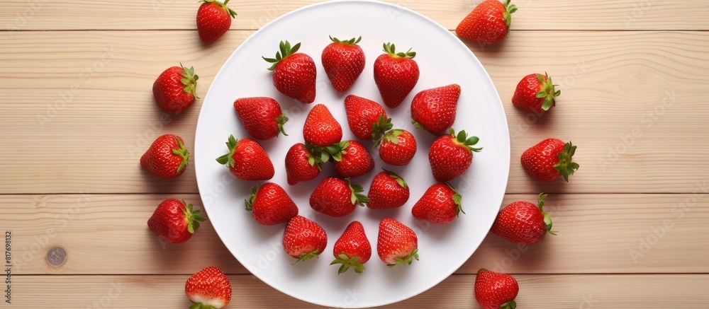 A close up top view of strawberries arranged on a white plate set against a wooden background Offers ample copy space for adding text A close up top view of strawberries arranged on a white plate set against a wooden background Offers ample copy space for adding text