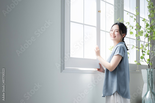 Woman standing at window looking up toward the outside Image of relaxing and waking up early in the morning sun Short sleeves in spring and summer