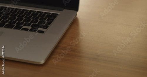 A man is about to open his laptop placed on a wooden table under bright indoor lighting.