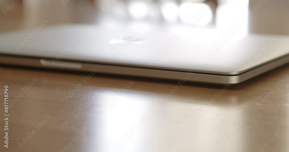 A man is about to open his laptop placed on a wooden table under bright indoor lighting. A man is about to open his laptop placed on a wooden table under bright indoor lighting.