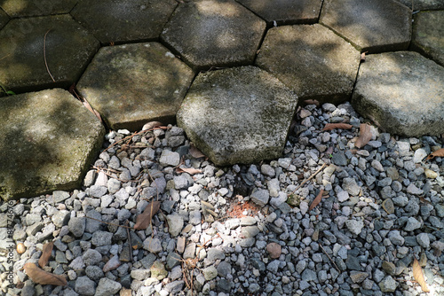 outdoor concrete paving floor with a hexagon shape, filled with moss, with a little gravel beside it © Adipra
