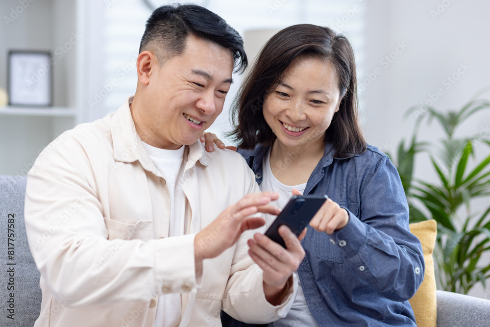 Happy couple using smartphone together at home, sharing joyful moments and enjoying technology. Relaxing and bonding in a cozy living room setting. Happy couple using smartphone together at home, sharing joyful moments and enjoying technology. Relaxing and bonding in a cozy living room setting.