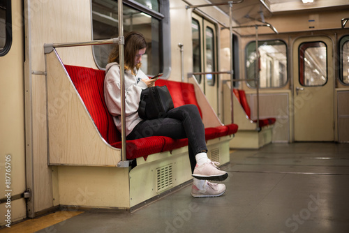 A young woman rides in a modern subway car with a phone in her hands. A beautiful girl in sweater rides after work in the subway with a smartphone in a half-empty car.