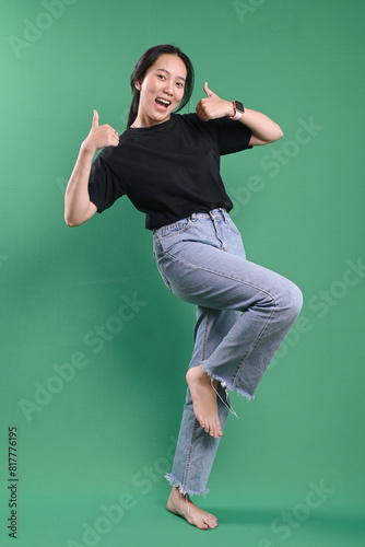 Beautiful young Asian woman with thumbs up showing recommendation sign on green background