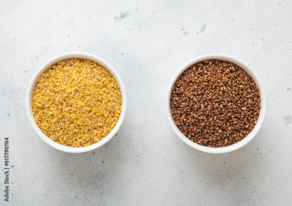 Ceramic bowls with brown and yellow bulgur dry raw seeds on kitchen table.Macro. Ceramic bowls with brown and yellow bulgur dry raw seeds on kitchen table.Macro.