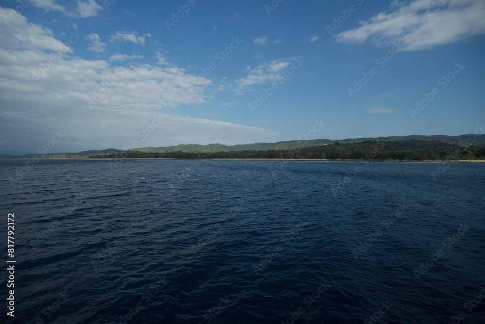 Expansive view of a calm blue ocean with a distant shoreline under a partly cloudy sky. Expansive view of a calm blue ocean with a distant shoreline under a partly cloudy sky.