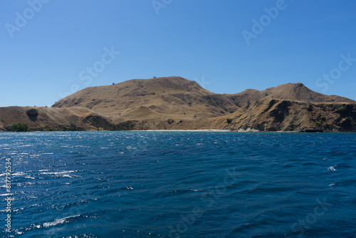 Serene coastal landscape with a clear blue sea and rolling golden hills under a bright sky