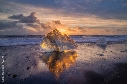 Reflection of an Ice fragment on black sand beach illuminated orange by a setting sun in Iceland
 photo