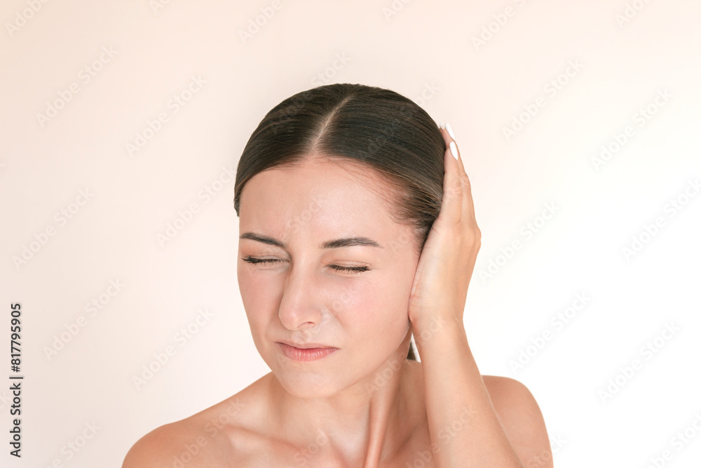 Young caucasian brunette woman is experiencing acute pain in her ear. She presses her ear with her hand, suffering from otitis. Isolated on a beige background Young caucasian brunette woman is experiencing acute pain in her ear. She presses her ear with her hand, suffering from otitis. Isolated on a beige background