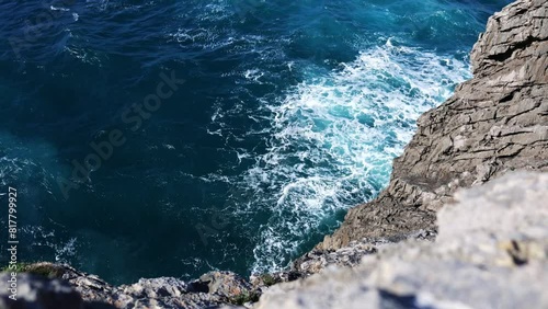 High angle shot of a rocky cliff, with waves crashing in slow motion. Travel, nature and wallpaper concept.