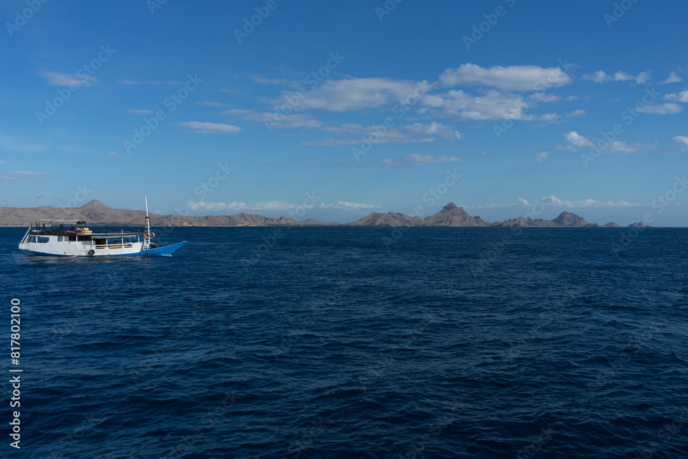 A boat sailing on the tranquil blue ocean against a backdrop of distant mountains under a clear sky. A boat sailing on the tranquil blue ocean against a backdrop of distant mountains under a clear sky.