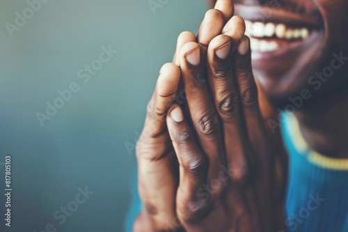 Close-up of a person smiling with hands clasped together in a gesture of gratitude or prayer. Background is blurred for focus on hands and expression.