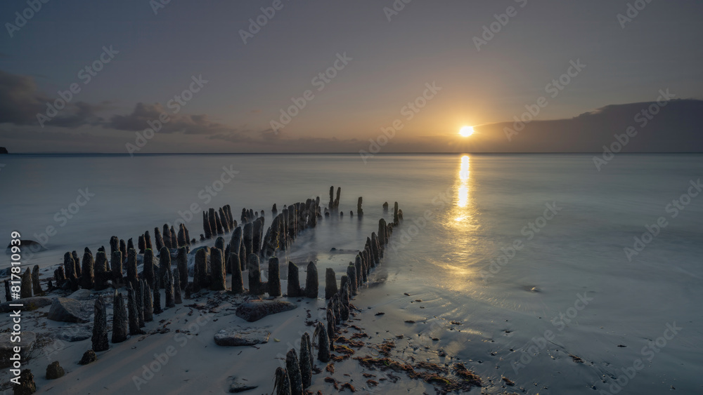 Obraz premium Scenic view of wooden pillars on the beach against the sea at sunset