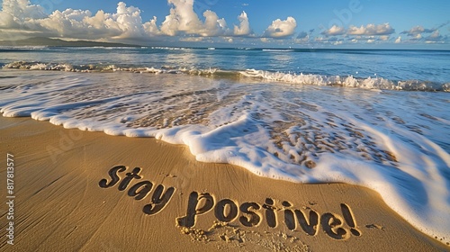 A picturesque beach scene with "Stay positive!" carved in large letters into the golden sand, waves gently lapping nearby