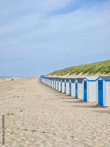 A vibrant row of beach huts line the sandy beach under a clear blue sky, adding a splash of color to the serene seascape.