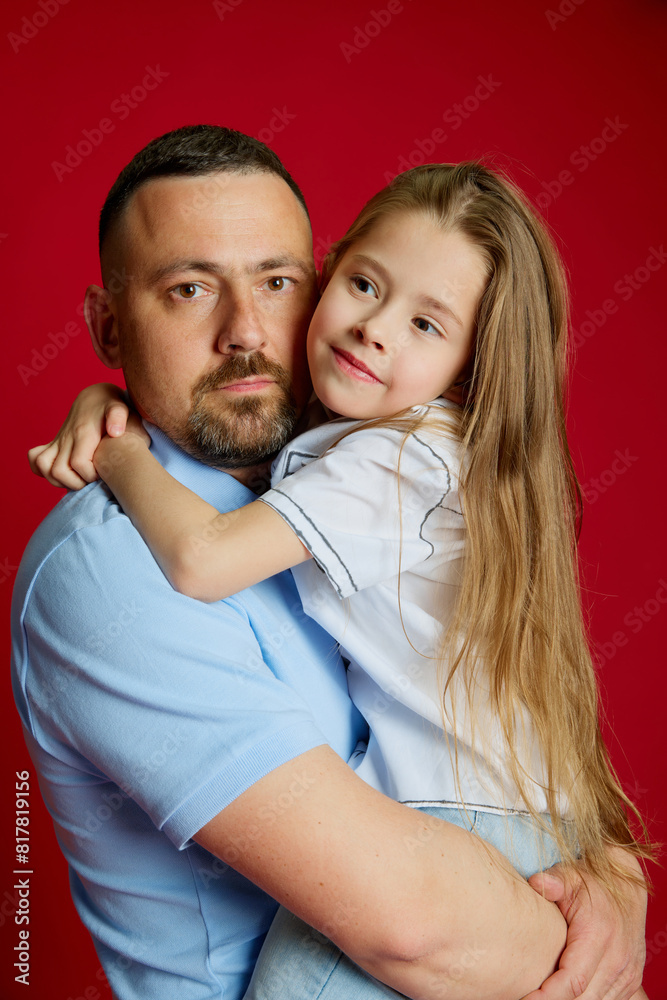 Portrait of young man holds on hands his beloved little daughter against vibrant red studio background. Father's love Concept of Father's day. Children's day, Family day, parenthood. Ad Portrait of young man holds on hands his beloved little daughter against vibrant red studio background. Father's love Concept of Father's day. Children's day, Family day, parenthood. Ad