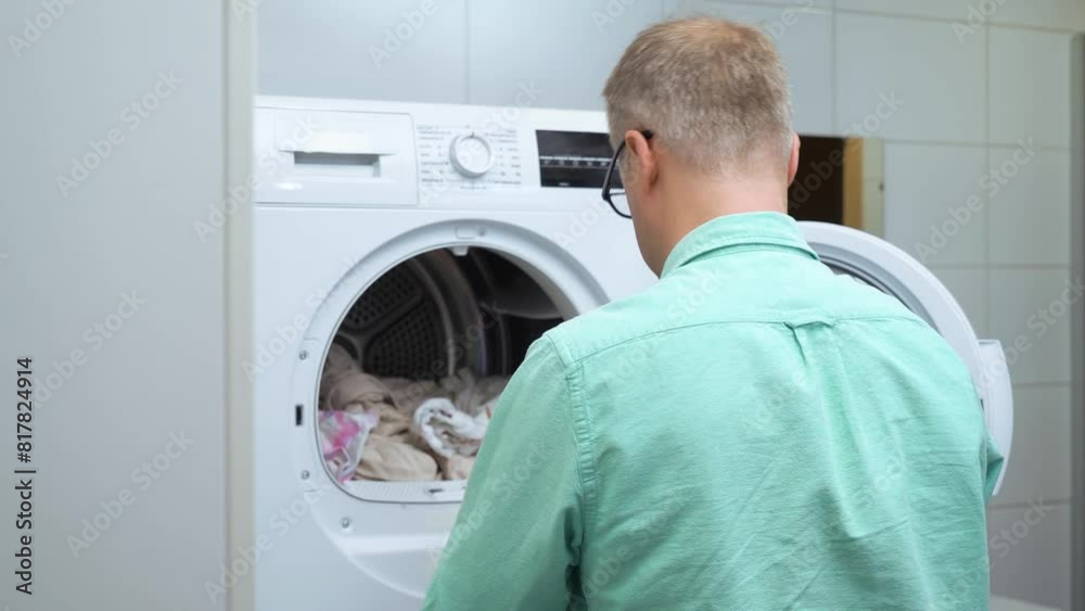 Middle-aged man loading clothes into the washing machine or dryer. Laundry cleaning. Housework, homework, male housekeeper. Husband man doing laundry at home. Washer and dryer at home. Middle-aged man loading clothes into the washing machine or dryer. Laundry cleaning. Housework, homework, male housekeeper. Husband man doing laundry at home. Washer and dryer at home.