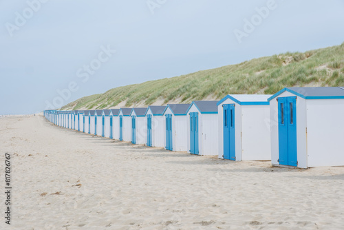 A peaceful scene unfolds as a row of charming blue beach huts stand tall against the sandy backdrop of Texel, Netherlands. De Koog beach Texel