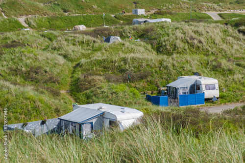 A serene scene where a group of RVs are peacefully parked on a grassy hillside in Texel, Netherlands, blending harmoniously with the natural beauty surrounding them.