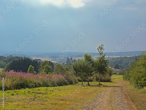 Ardennes landnscape with hills trees and pink loosetrife flowers and towers of the Basilica of Saint-Hubert in the evening sun. Luxembourg, Wallonia, Belgium 