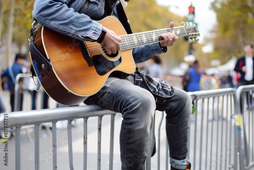 musician sitting on metal barrier playing guitar outdoors photo