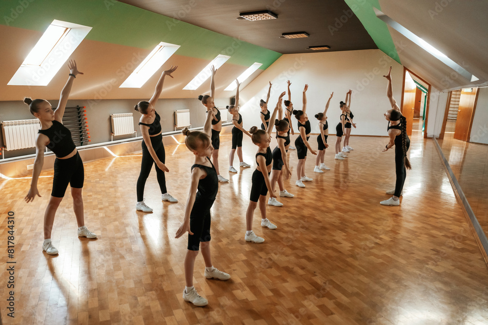 Fototapeta premium Side view. Group of female kids practicing athletic exercises together indoors