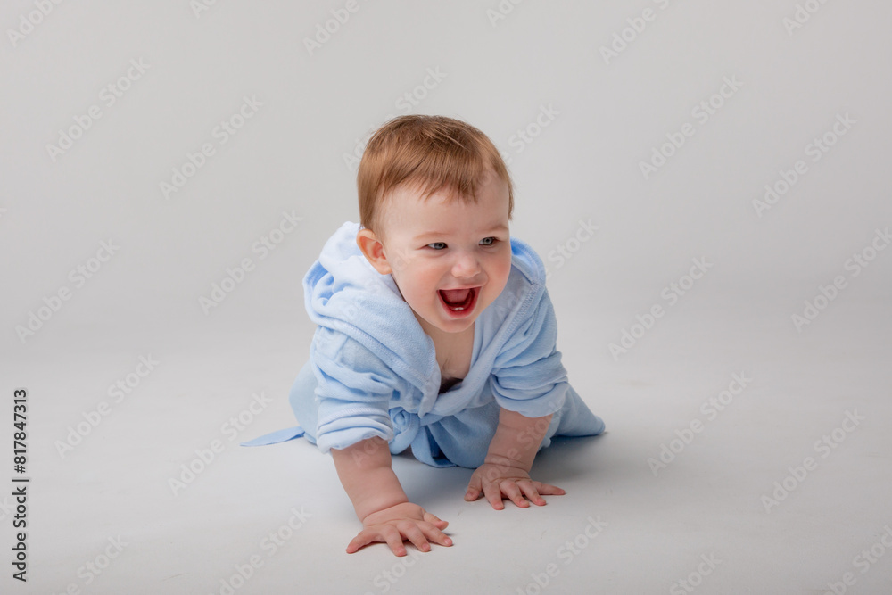 A cute happy laughing baby in a soft bathrobe crawls on a white background after bathing. The child is wrapped in a clean and dry towel. Washing, baby hygiene, health and skin care A cute happy laughing baby in a soft bathrobe crawls on a white background after bathing. The child is wrapped in a clean and dry towel. Washing, baby hygiene, health and skin care