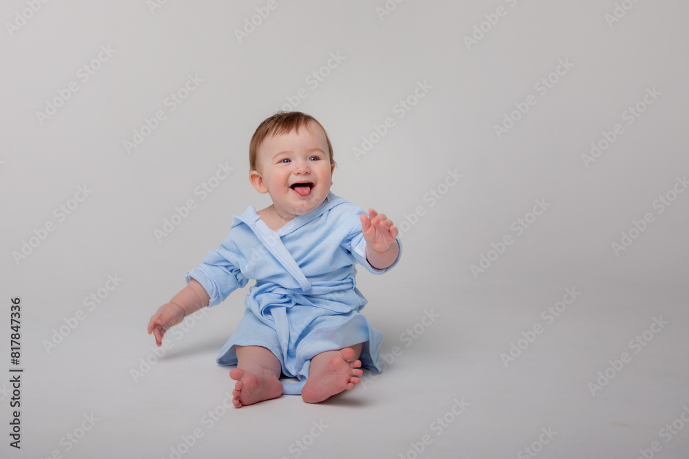 Cute happy laughing baby in a soft bathrobe after bathing plays on a white background. The child is wrapped in a clean and dry towel. Washing, baby hygiene, health and skin care Cute happy laughing baby in a soft bathrobe after bathing plays on a white background. The child is wrapped in a clean and dry towel. Washing, baby hygiene, health and skin care
