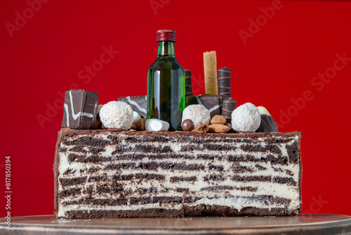 Chocolate cake with candies and small bottle whiskey Jameson for a birthday gift for a man, close-up, red background