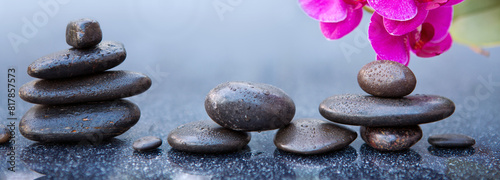 Pink orchid flowers and black spa stones on the gray table background.