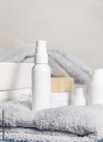 White blank spray bottle on grey folded towel near other cosmetics and basin, mockup