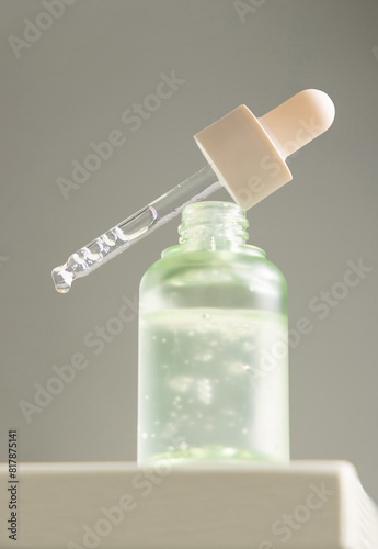 Drop falls from a pipette resting on a bottle filled with green serum agains gray, macro