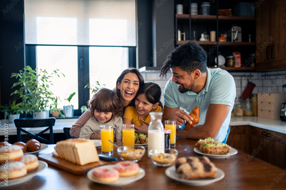 Two happy kids, boy and girl enjoying eating breakfast with parents. Smiling beautiful mother laughing and having fun with her kids and husband during breakfast at home.