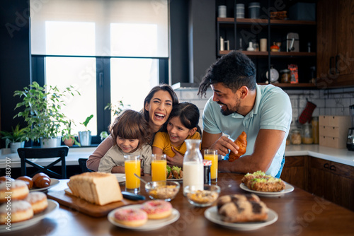 Two happy kids  boy and girl enjoying eating breakfast with parents. Smiling beautiful mother laughing and having fun with her kids and husband during breakfast at home.