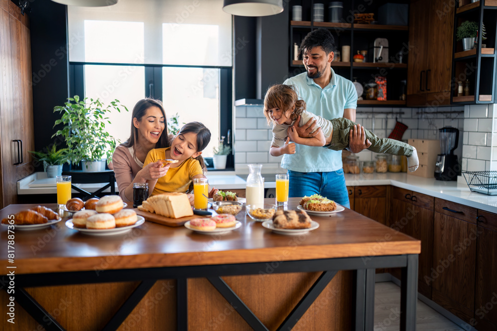 Young parents with small children having fun during breakfast. Mother and father at breakfast with son and daughter in the kitchen at home. Young parents with small children having fun during breakfast. Mother and father at breakfast with son and daughter in the kitchen at home.