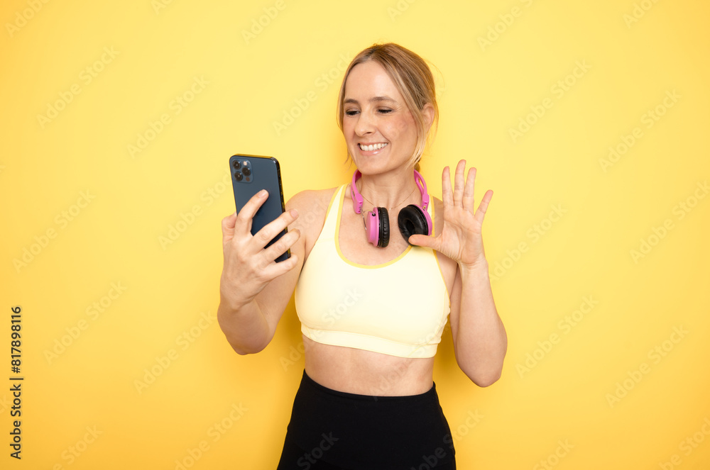 Young athletic woman using mobile phone, standing against yellow background Young athletic woman using mobile phone, standing against yellow background
