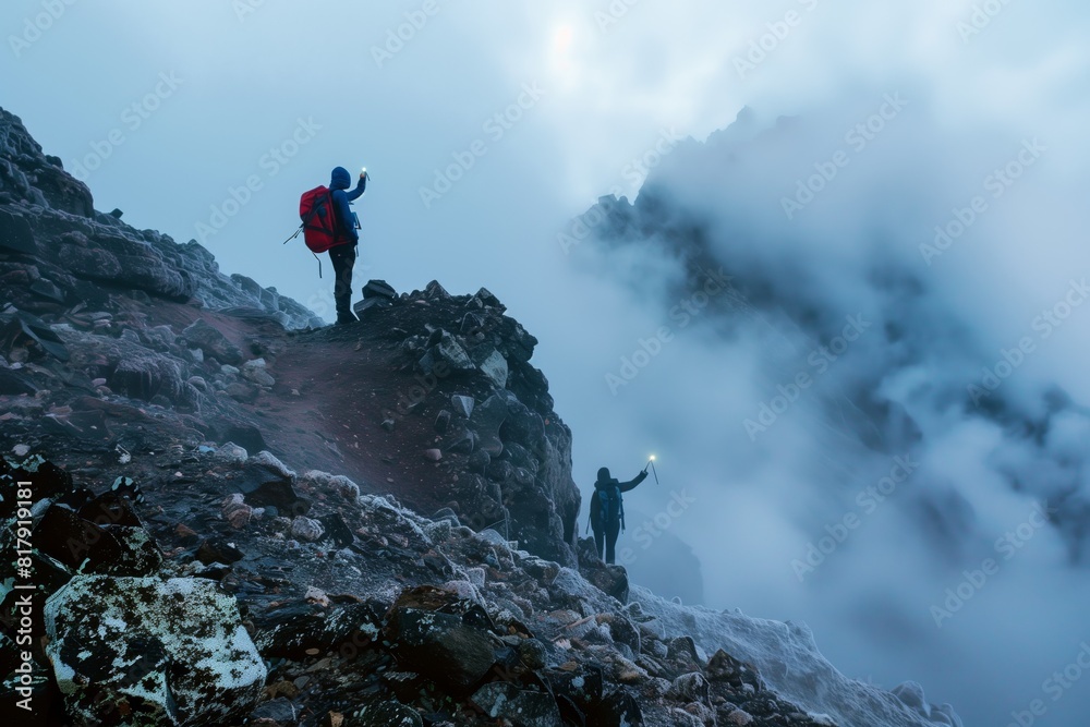 Fotografie Two hikers with backpacks navigate a rocky, foggy mountain terrain using flashlights