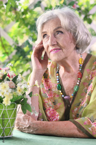 Beautiful elderly woman sits at a table in the summer at the country house