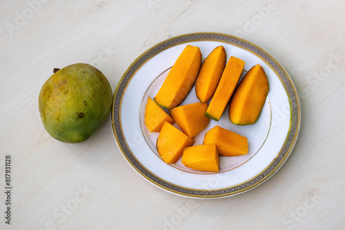 Peeled mango slices on a white plate on wooden background, a whole ripe mango placed beside 