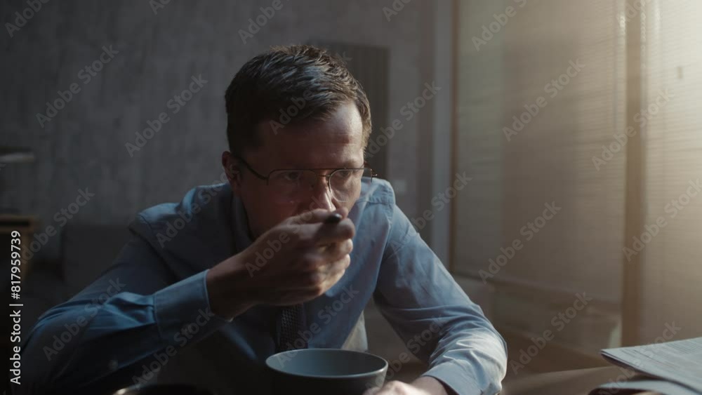 A man in a blue shirt slowly eats cereal A man in a blue shirt slowly eats cereal