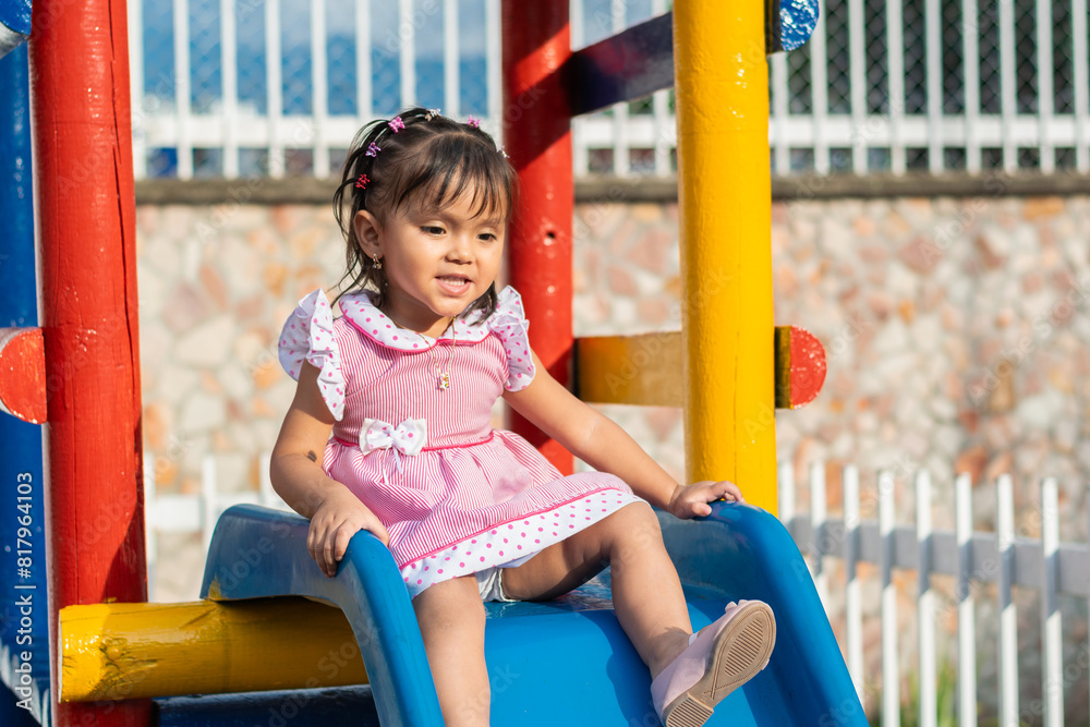 happy little brunette latina girl smiling at the top of the little slippery slide looking down. happy little brunette latina girl smiling at the top of the little slippery slide looking down.