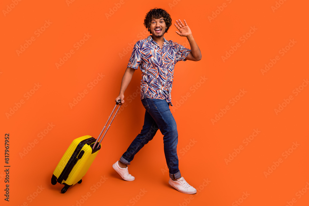 Full length photo of handsome young man baggage walk wave hand dressed stylish colorful garment isolated on orange color background Full length photo of handsome young man baggage walk wave hand dressed stylish colorful garment isolated on orange color background