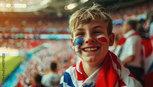 A happy English boy fan with face painted in the colors of England flag is posing at stadium while cheering for his team during football match, fans around him