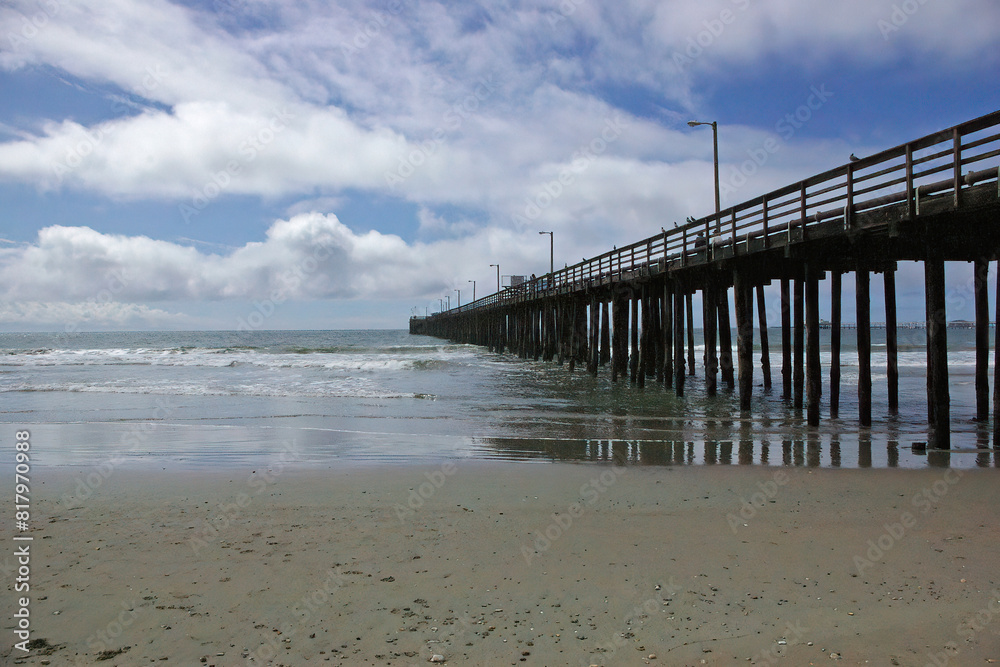 Ocean beach and a pier under a vivid blue sky with clouds