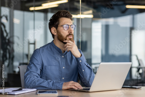 Foto A serious and pensive young man is sitting in the office at a desk with a laptop