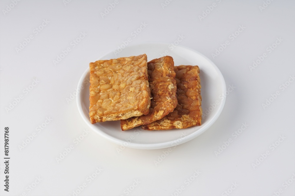 pieces of fried tempeh on a white plate on a white table with studio lighting pieces of fried tempeh on a white plate on a white table with studio lighting