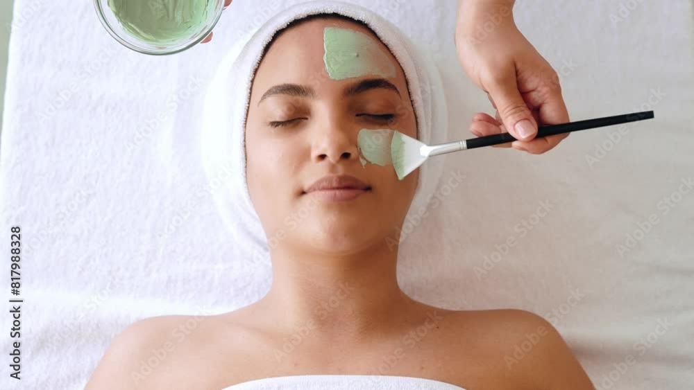 Close-up of beauty procedure, therapist applying green face mask on half face of a gorgeous brazilian or hispanic young woman. Skin care concept. Facial treatments, facial cleansing