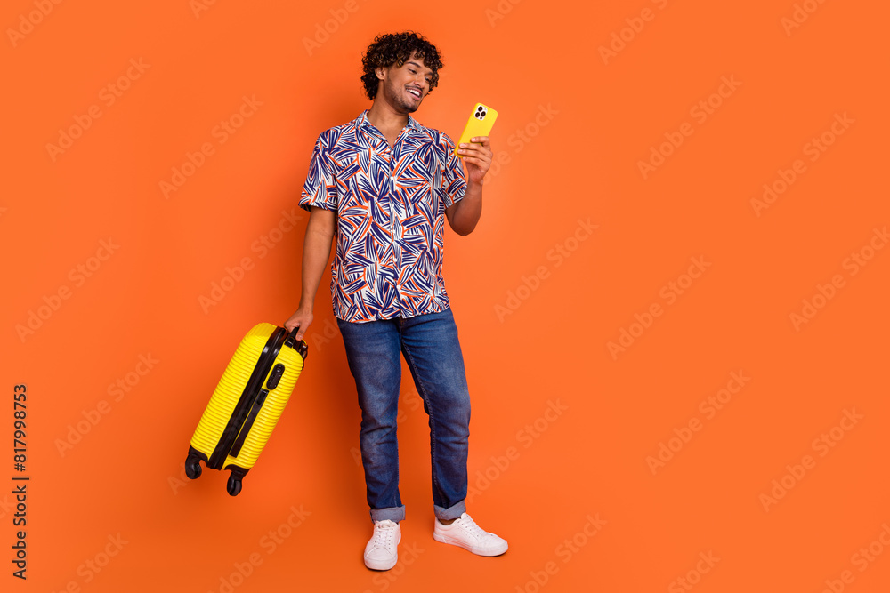 Full length photo of handsome young man hold baggage device dressed stylish colorful garment isolated on orange color background Full length photo of handsome young man hold baggage device dressed stylish colorful garment isolated on orange color background